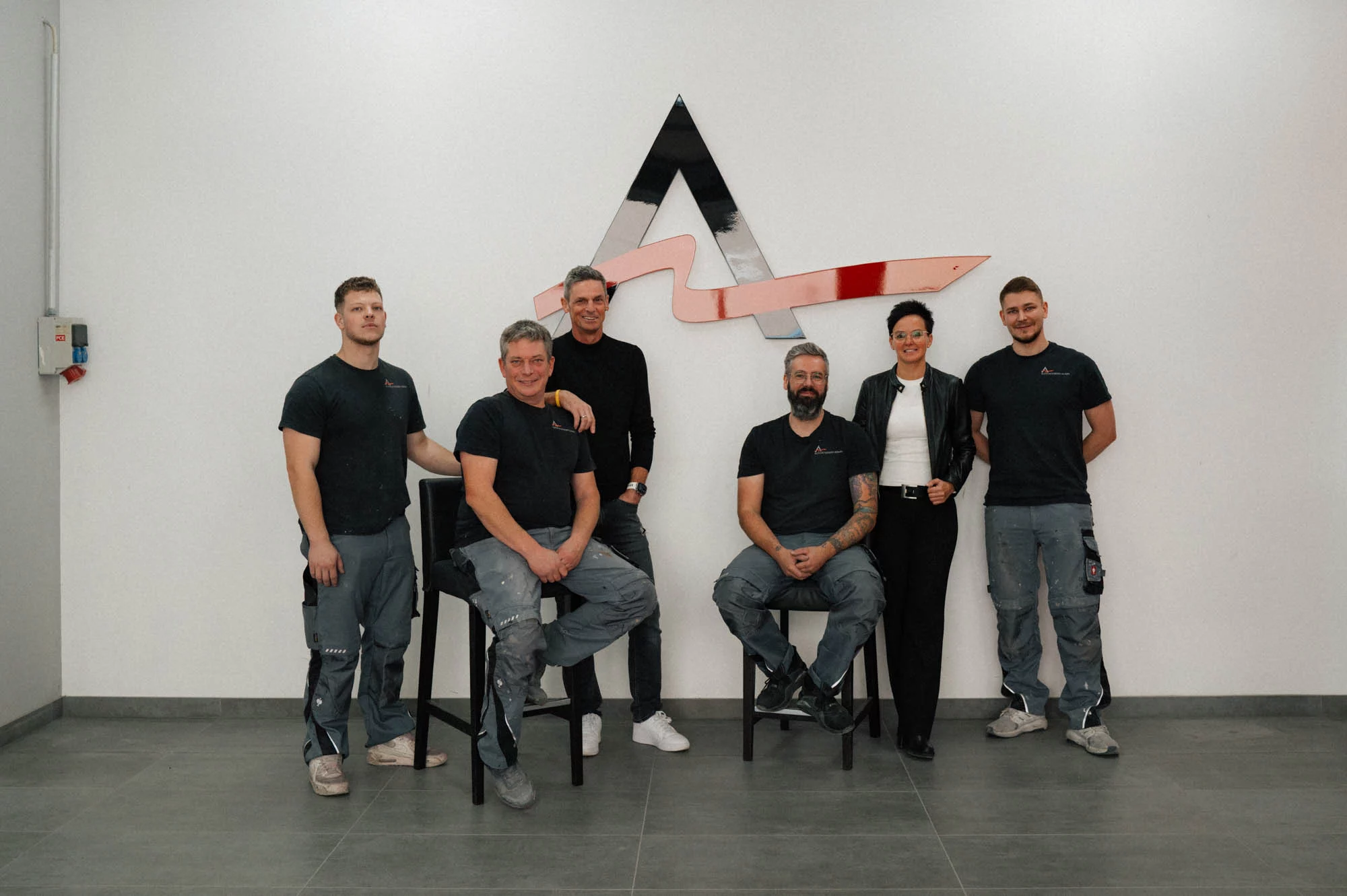 Das Team der Autolackiererei Adams vor dem Firmenlogo